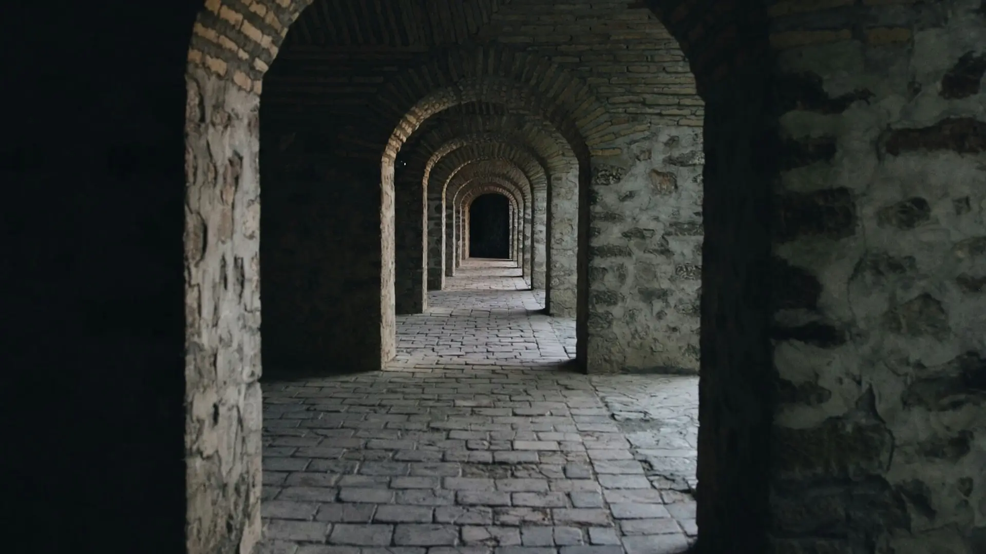 Serie di archi oscuri immersi nelle ombre, con un fascio di luce che illumina leggermente il percorso, simbolo di introspezione e scoperta interiore.
